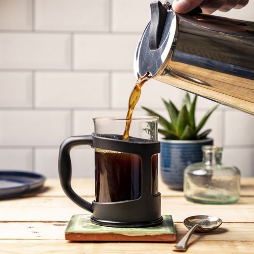 A closeup shot of a person pouring coffee into a glass cup in the kitchen