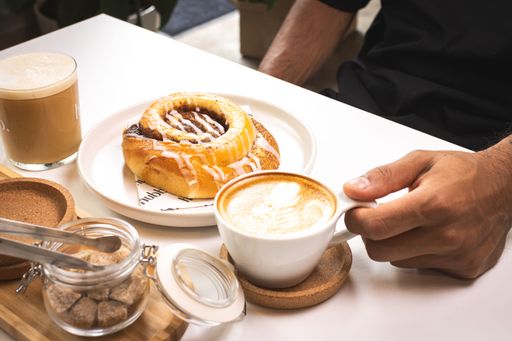 A closeup of a white mug of latte coffee with several colorful wooden coffee stirrers and a cookie