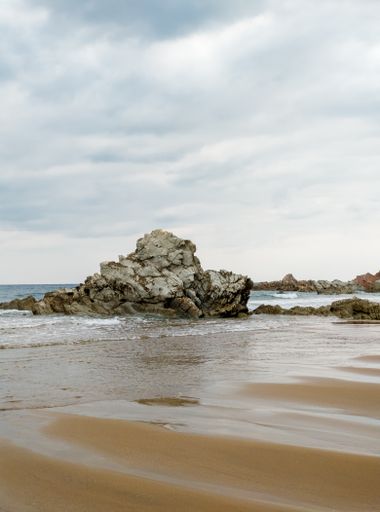 A vertical shot of rocks on the beach of Sopelana under a cloudy sky in Spain