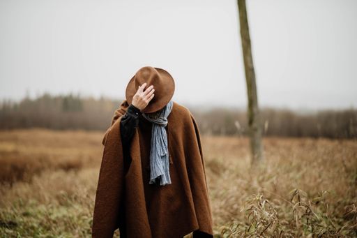 A man in a brown fedora and poncho standing in a field