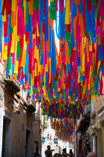 A vibrant scene of a bustling city street with a multitude of colorful paper streamers adorning the buildings and festive atmosphere