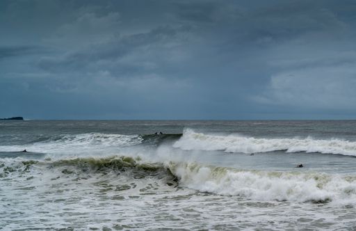 A photo of waves and surfers in Alexandra Headland Beach under dark cloudy skies