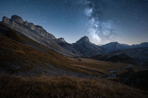 Landscape view of the milky way over dry meadows and a mountain range in the background, shot at the Col du Sametsch in Wallis Switzerland