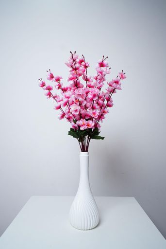 An elegant white ceramic vase on a classic wooden table, filled with delicate pink flowers, creates a stunning visual composition