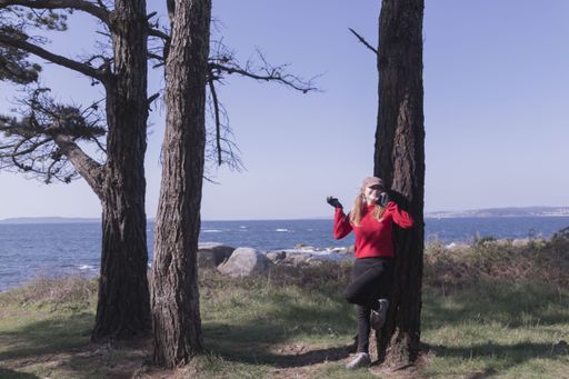 A happy european female leaning on a tree and talking with her phone