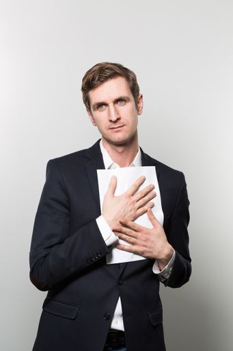 A vertical shot of a well-dressed male holding a piece of paper against his chest
