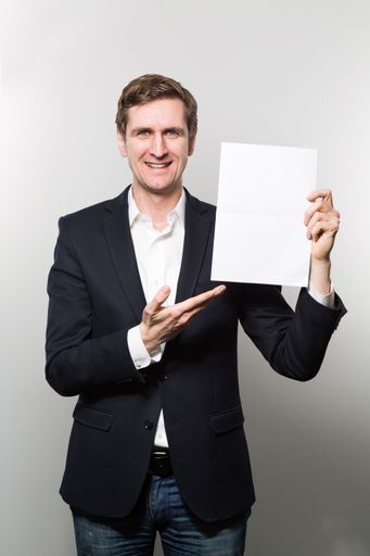 A vertical shot of a well dressed male smiling while pointing to a paper that he is holding