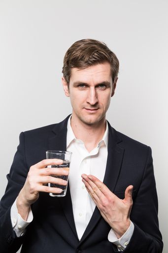A vertical shot of a well-dresed male pointing to a glass of water that he is holding