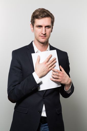 A vertical shot of a well-dressed male holding a piece of paper against his chest