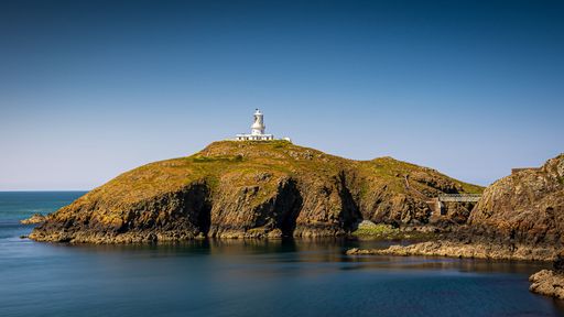 A white lighthouse atop a rocky cliff overlooking a vast blue ocean in Strumble Head