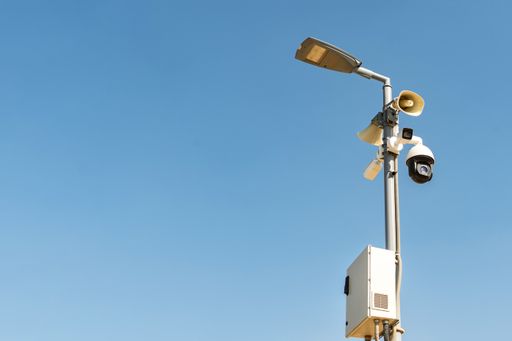 A cluster of security cameras on a lamppost, in a public Park on the sky background, with copy space
