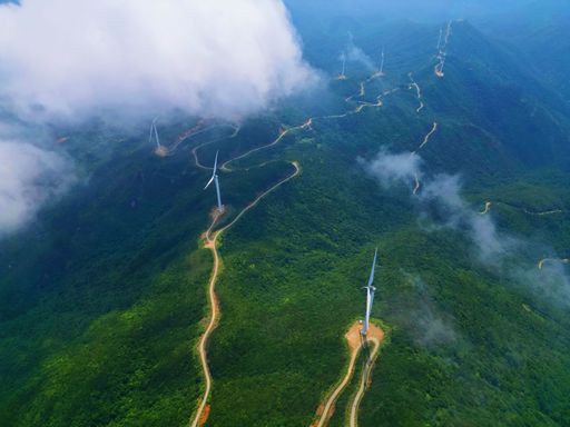 A picturesque landscape of a rolling hillside covered in trees and wind turbines dotting the horizon