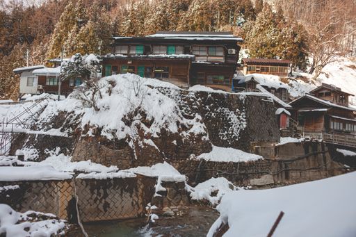 A beautiful shot of a wooden house on the cliff near trees covered in snow in the winter