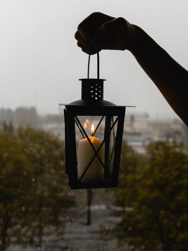 A vertical shot of a hand holding a vintage lamp with a lit candle