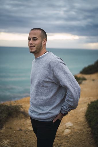 A young man smiling and standing on a cliff near the beautiful sea