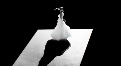 A woman wearing a white bridal gown dancing illuminated in a dark atmosphere