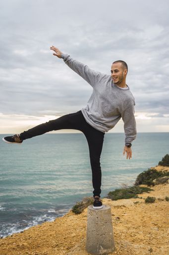 A vertical shot of a young man standing on a stone near the sea trying to balance himself