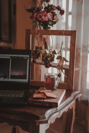 A vertical shot of a laptop, a glass of tea, and cookies on a working table in the room