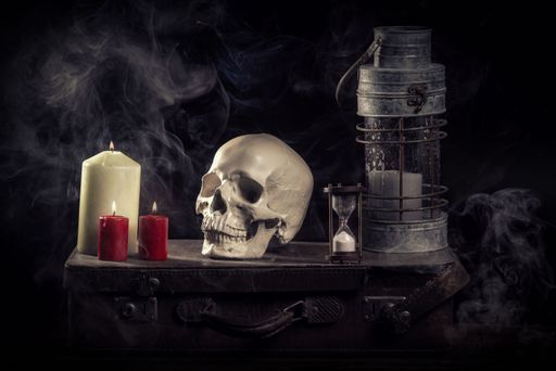 A spooky shot of a human skull on a trunk with candles, an hourglass and smoke