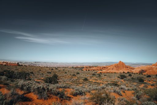 A scenic view of red sand dunes and mountains against a bright blue sky in Arches National Park