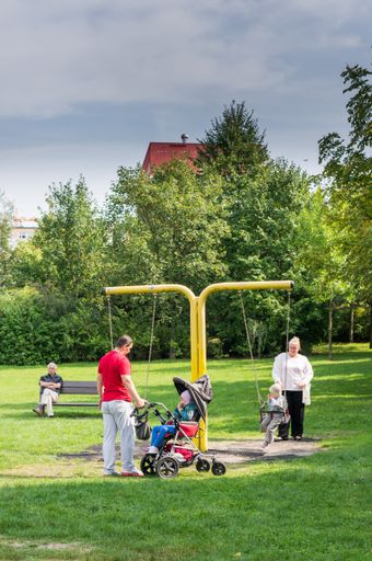 Man and woman with two children including one disabled in a buggy by a swing set on a playground.