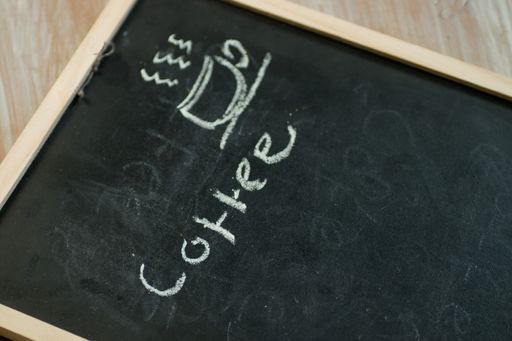 A closeup of a chalkboard with a handwritten "coffee" word and a drawing of a steaming coffee mug