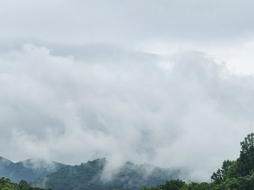 A scenic view of a winding, unpaved road leading through a lush, green landscape with a snow-capped mountain range in the background