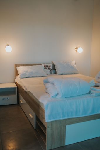 A vertical shot of a bright modern room with tiled floor, lamps, and a bed that has a cat-printed pillow on it