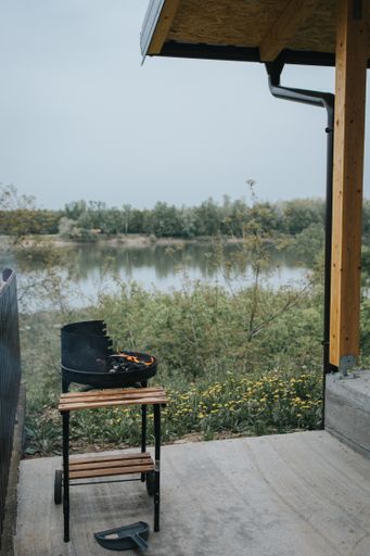 A fire pit on wooden surface outside the house with a lake and field of flowers in the background
