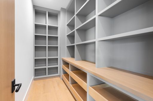 A spacious white-walled closet with wooden shelves and open shelving units, providing ample storage space