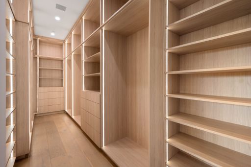 An interior shot of a luxurious walk-in closet featuring an oak floor and two walls with multiple shelves for storage