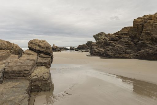 A huge natural rock formations on a sandy As Catedrais beach on a gloomy day in Lugo, Spain