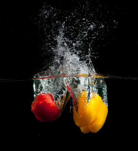 A stunning image of two brightly colored peppers submerged in a body of water with a splash visible in the background