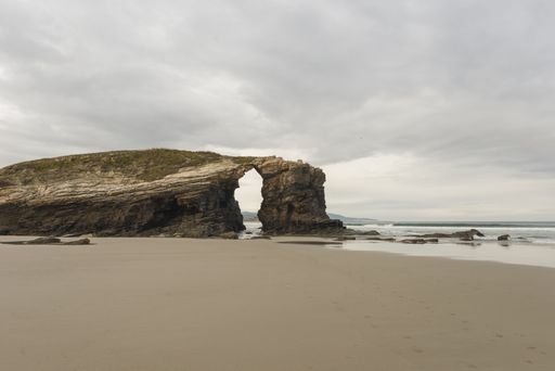 A giant natural rock formations on a sandy As Catedrais beach on a gloomy day in Lugo, Spain