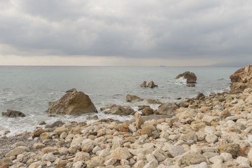 A landscape of the Penon del Cuervo Beach surrounded by the sea under a cloudy sky in Spain