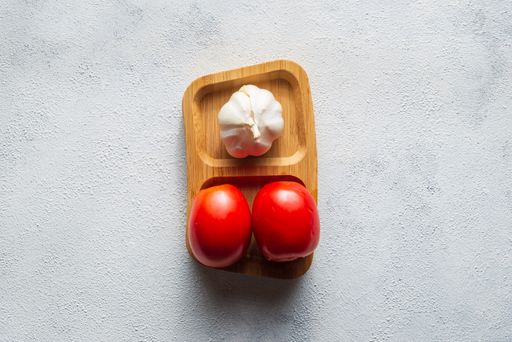 A top view of tomatoes and garlic on a wooden plate on a white surface