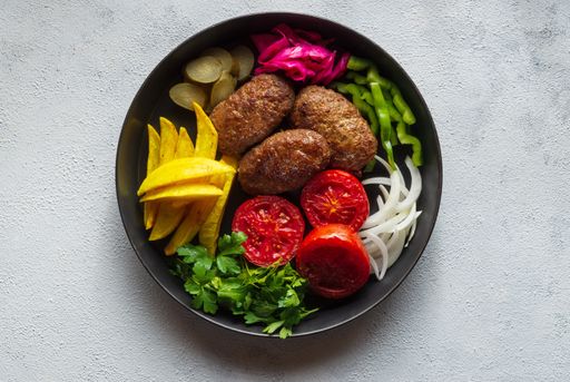 A top view of meat cutlets and vegetables on a black plate on a white surface