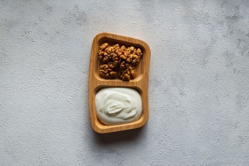 A top view of mayo and walnuts on a wooden plate on a white surface