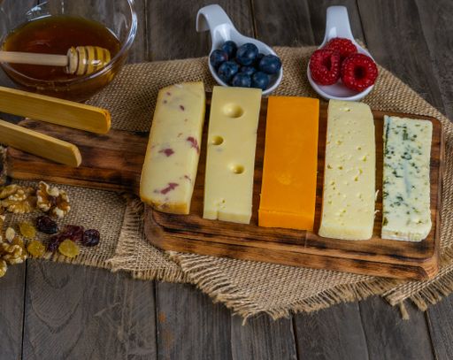 assorted cheese board with honey, nuts, blueberries and raspberries on wooden background