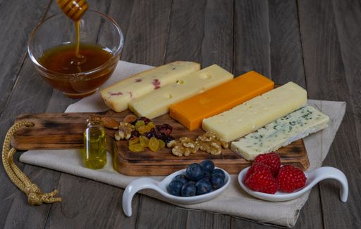 assorted cheese board with honey, nuts, blueberries and raspberries on wooden background