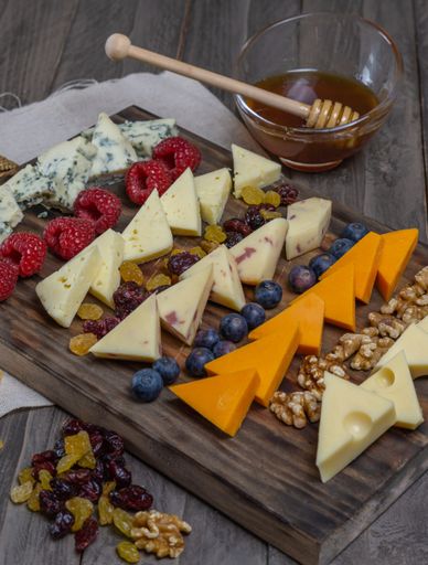 assorted cheese board with honey, nuts, blueberries and raspberries on wooden background