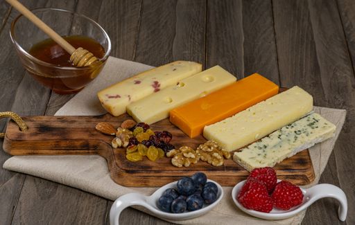 assorted cheese board with honey, nuts, blueberries and raspberries on wooden background