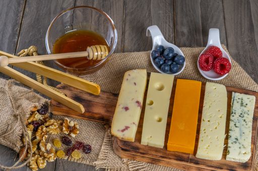 assorted cheese board with honey, nuts, blueberries and raspberries on wooden background
