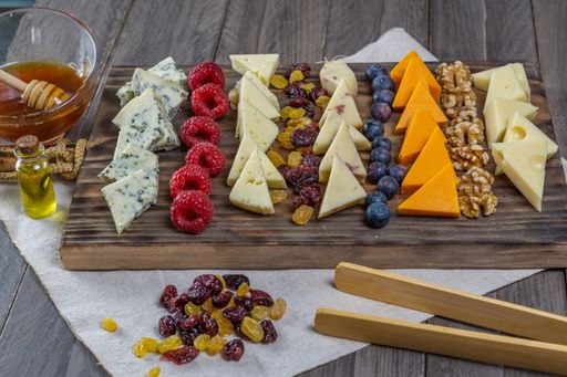 assorted cheese board with honey, nuts, blueberries and raspberries on wooden background