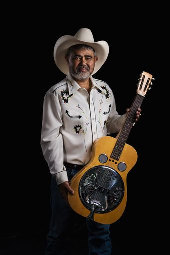 Portrait of bearded Asian musician dons cowboy attire, clutching a Dobro guitar, merging Americana and Eastern styles on a black backdrop