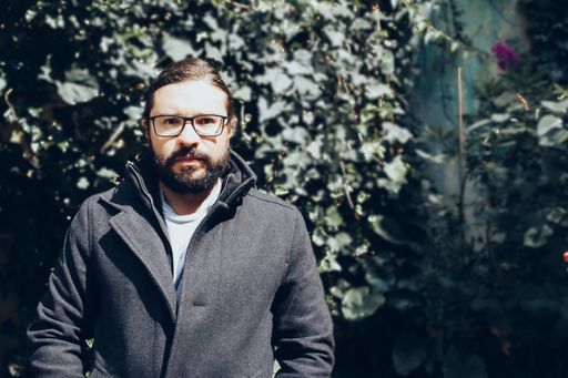 A bearded man in black jacket wearing eyeglasses with a blurred background