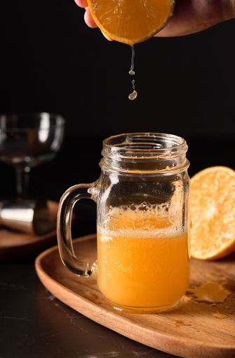 An interesting vertical shallow focus shot of orange juice being squeezed into a mason jar glass with bartending appliances in the background.