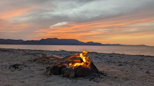 A tranquil sunrise scene featuring a beach bonfire burning at sunset