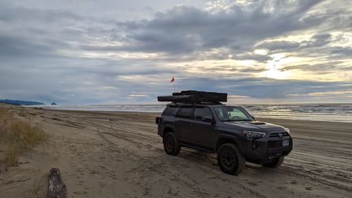 A closeup of a Toyota car  parked on a sandy beach beside the crystal blue water in the USA