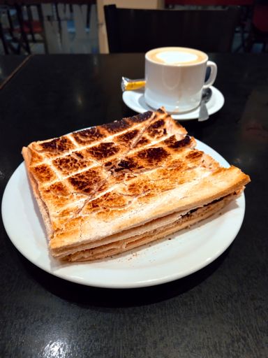 Delicious toasted ham and cheese sandwich crumbs halved in triangles on a white plate on a dark wooden table. Classic Argentine snack. High angle shot